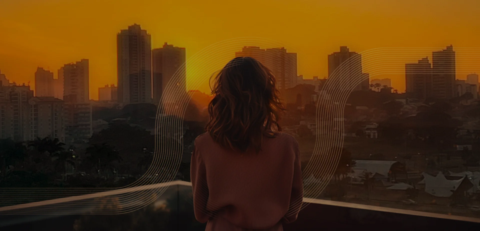 Mulher observando a cidade da varanda com a paisagem de prédios ao por do Sol